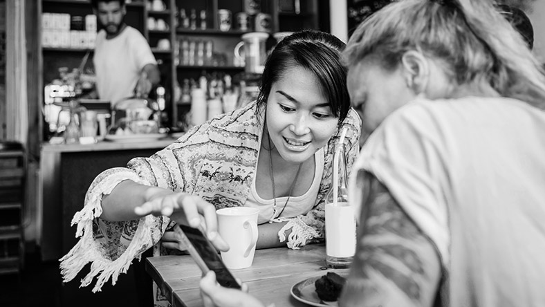 Two female friends using a smartphone to transfer money while out for coffee..